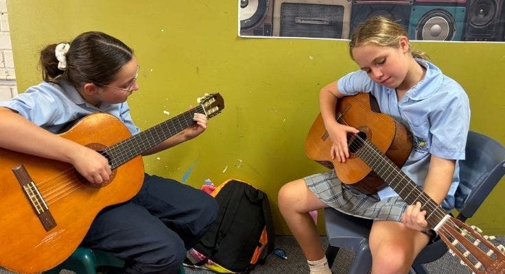 Two junior girls playing guitar in music lesson