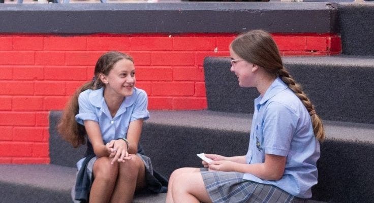 Two junior girl students sitting on step chatting